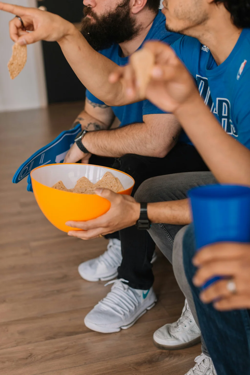 Friends watching a game together, eating chips and wearing sports team shirts